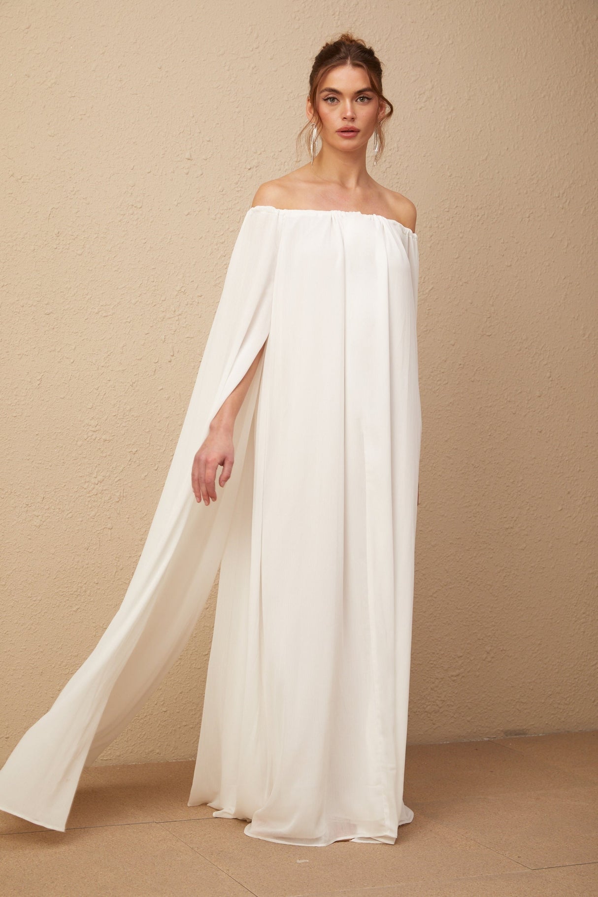 Woman wearing a flowing white tulle maxi dress with capelike design and draped details