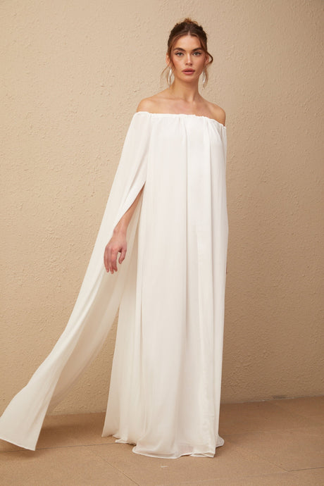 Woman wearing a flowing white tulle maxi dress with capelike design and draped details