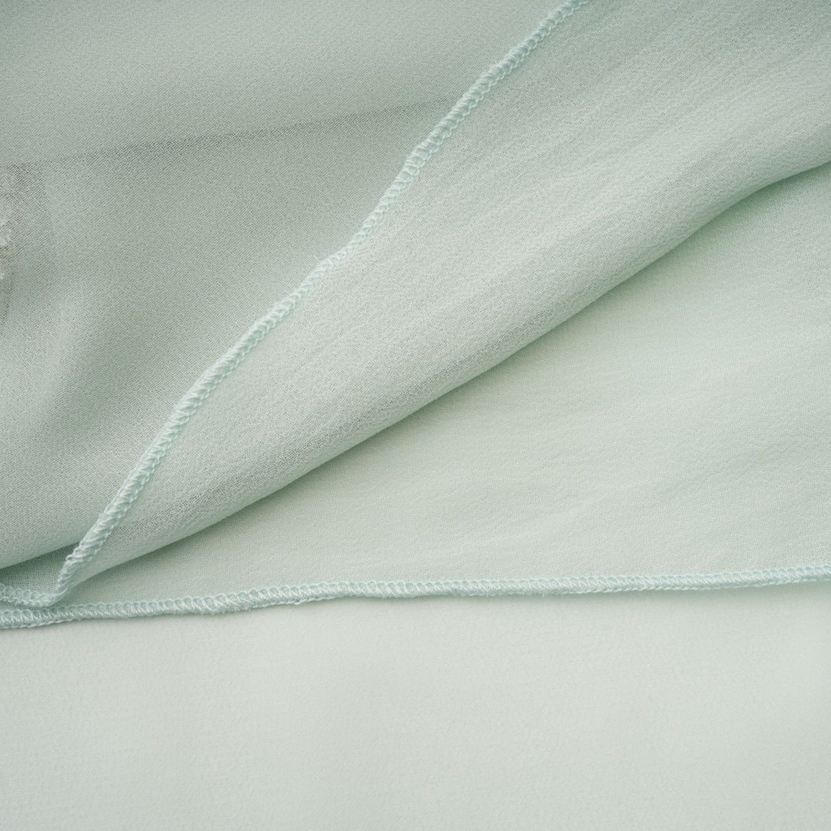 Woman wearing a flowy midi dress with ruffles and embellishments in a soft pastel color standing against a plain background