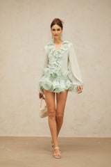 Woman wearing a green chiffon blouse with flounces and matching skirt from Noémie