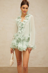 Woman wearing a green chiffon blouse with ruffles and matching skirt set from Noémie