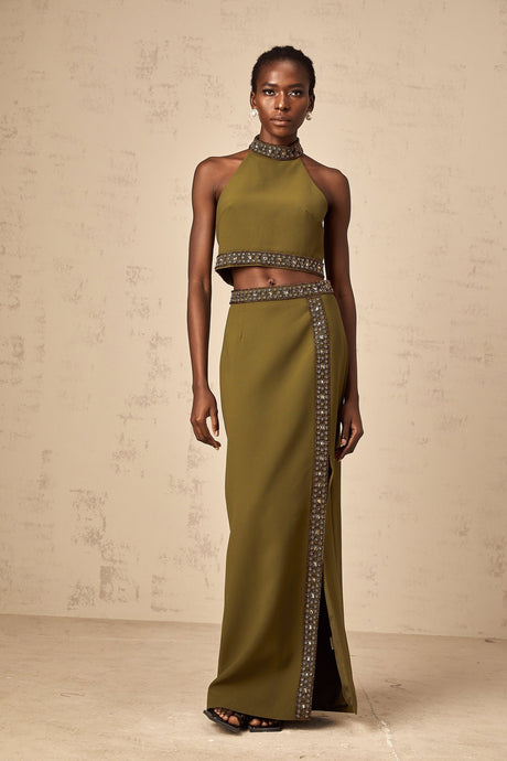 Woman wearing a green daisy print top and matching skirt with beaded trim details standing against a plain background