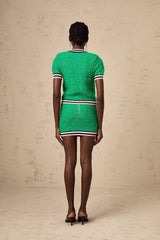 Woman wearing a green knitted top and matching skirt set standing against plain background