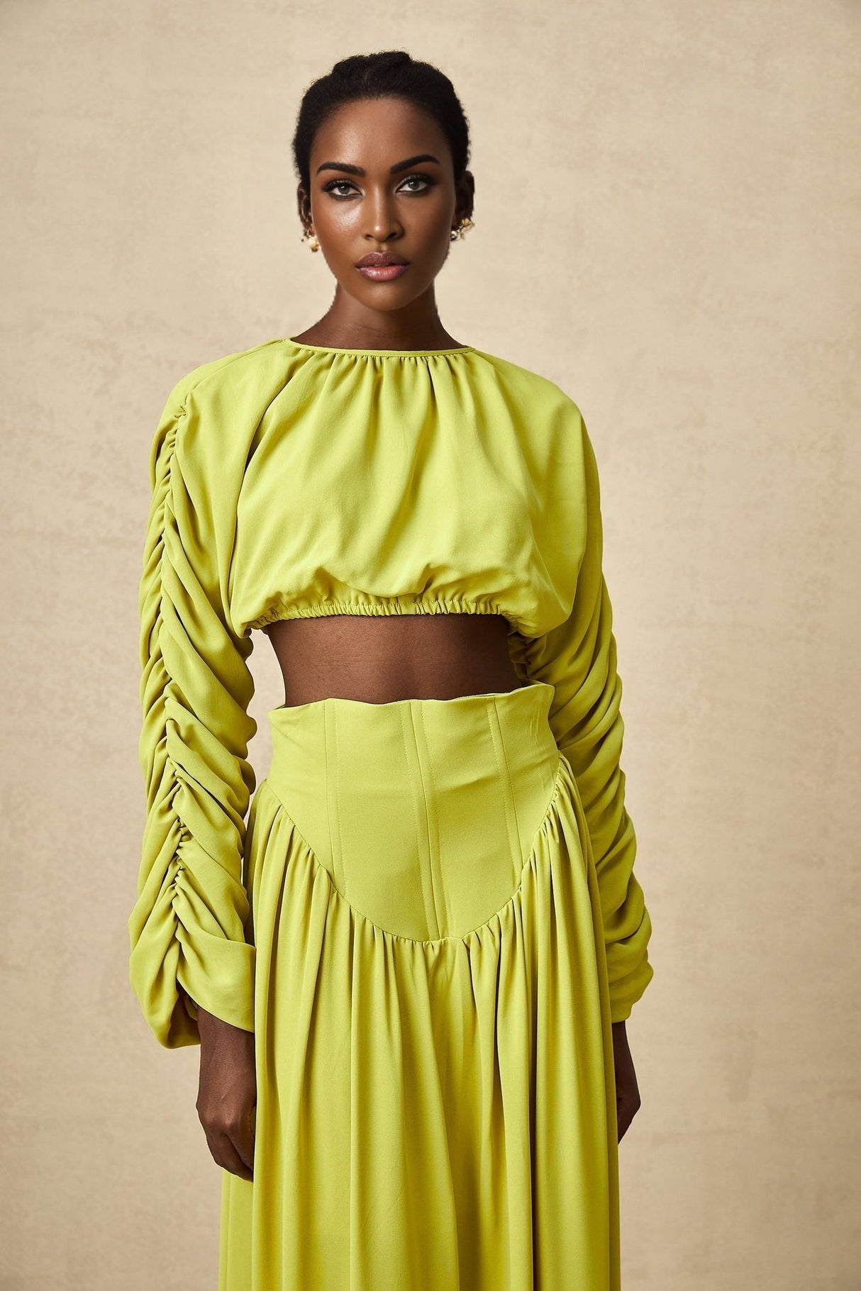 Woman wearing a green twopiece outfit consisting of a smocked top and matching skirt called Émilie