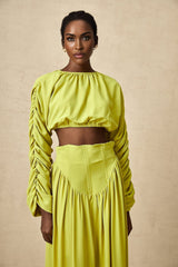 Woman wearing a green twopiece outfit consisting of a smocked top and matching skirt called Émilie