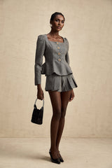 Woman wearing a grey herringbone patterned matching top and shorts set named Agathe The set features a short sleeve top paired with high waisted shorts in a textured herringbone fabric