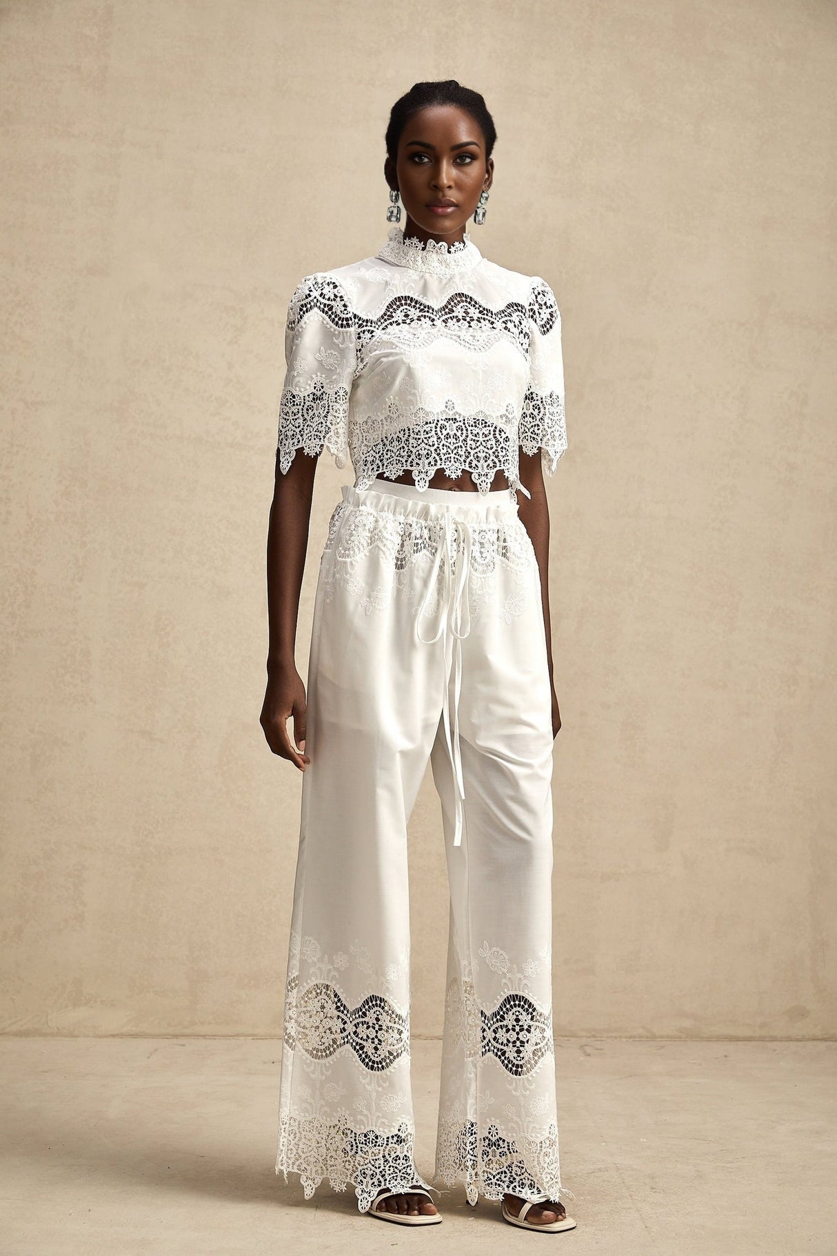 Woman wearing a lace trimmed cropped top and matching trousers with cutout details in a stylish two piece set