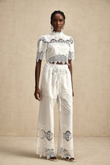 Woman wearing a lace trimmed cropped top and matching trousers with cutout details in a stylish two piece set