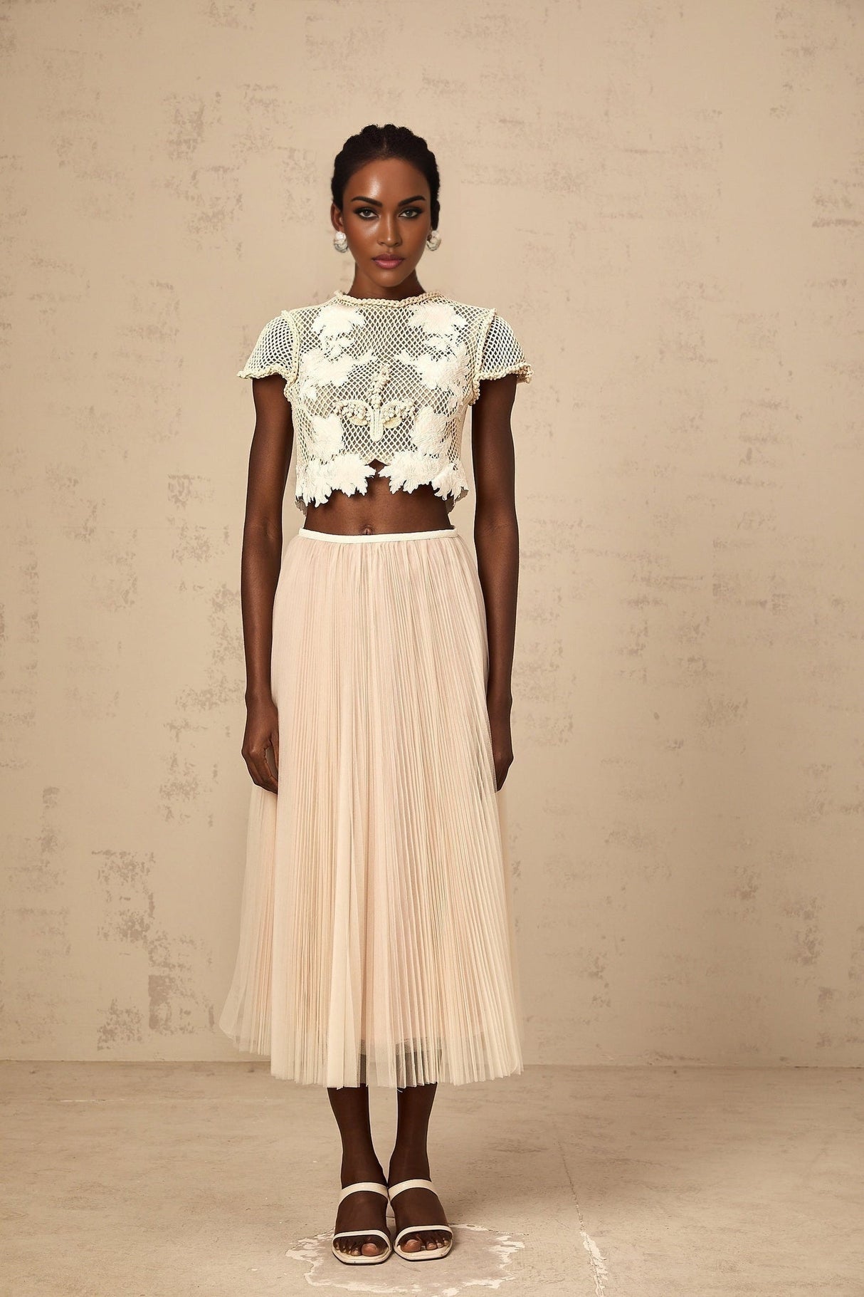 Woman wearing a light colored matching set with a top and skirt featuring floral applique details in neutral tones