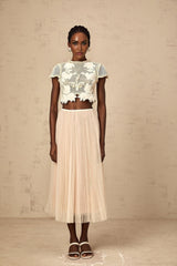 Woman wearing a light colored matching set with a top and skirt featuring floral applique details in neutral tones