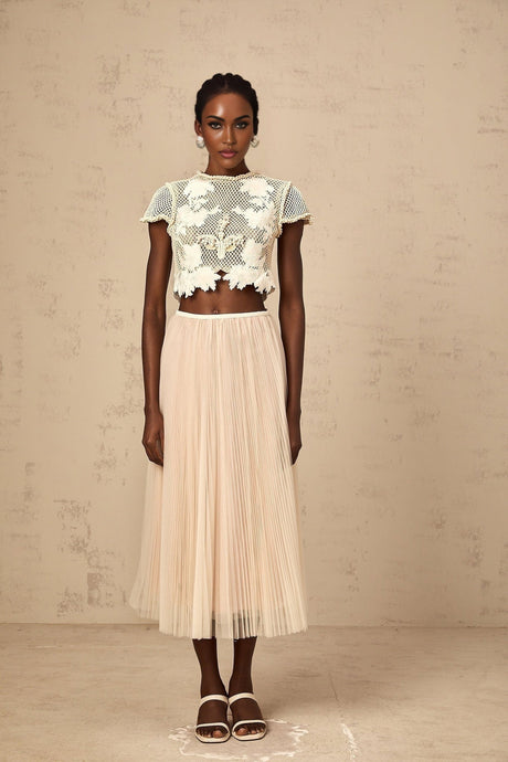Woman wearing a light colored matching set with a top and skirt featuring floral applique details in neutral tones