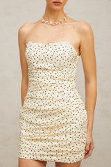Woman wearing a light colored mini dress with small polka dots and ruched detailing