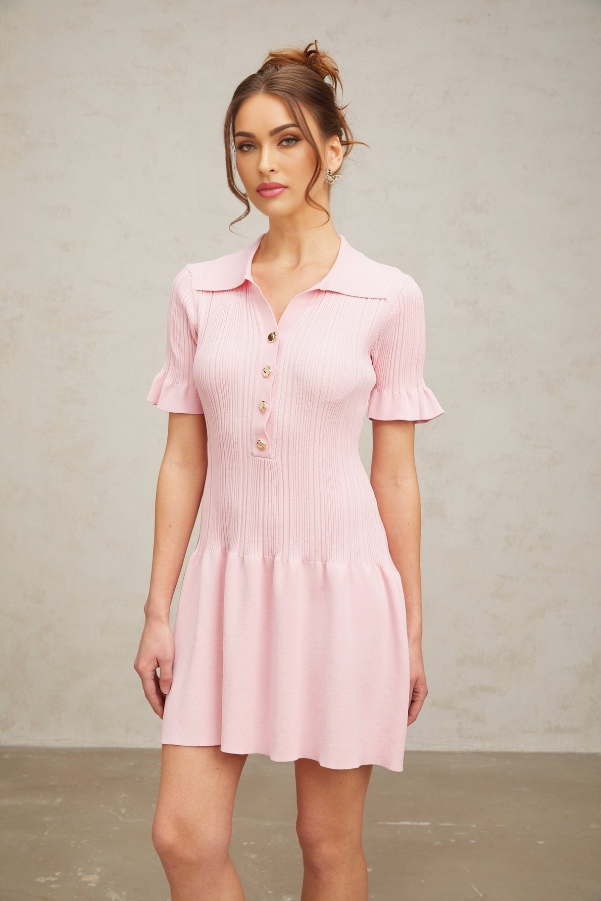 Woman wearing a light pink mini dress with a flared skirt and long sleeves made of fine knit fabric