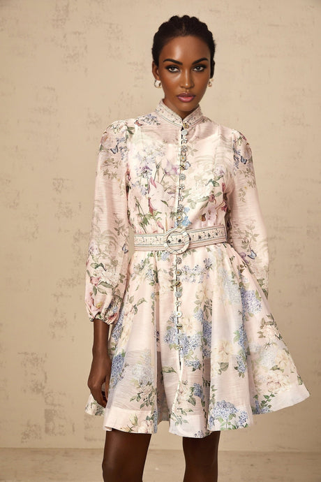 Woman wearing a light pink mini dress with a floral print pattern standing against a plain background