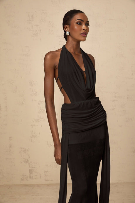 Woman wearing a long black halterneck maxi dress with open back design standing against plain background
