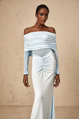 Woman wearing a long blue offshoulder dress with ruched details and flowing maxi length skirt
