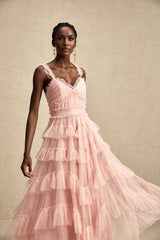 Woman wearing a long flowy layered maxi dress with ruffled tulle skirt in pale color standing against plain background