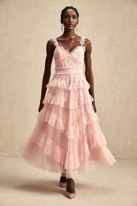 Woman wearing a long flowy maxi dress with multiple layers of ruffled tulle fabric in a soft color