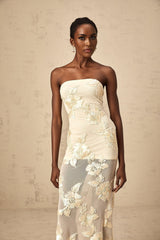 Woman wearing a long neutralcolored offshoulder maxi dress with embroidery details