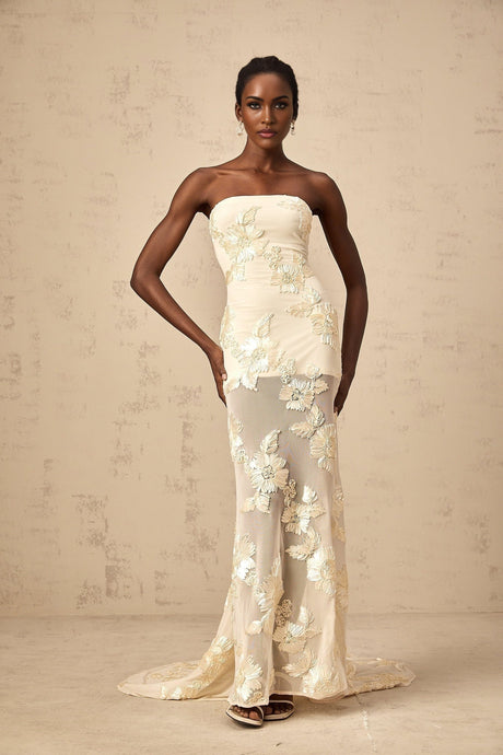 Woman wearing a long offshoulder maxi dress in neutral tones with embroidered details
