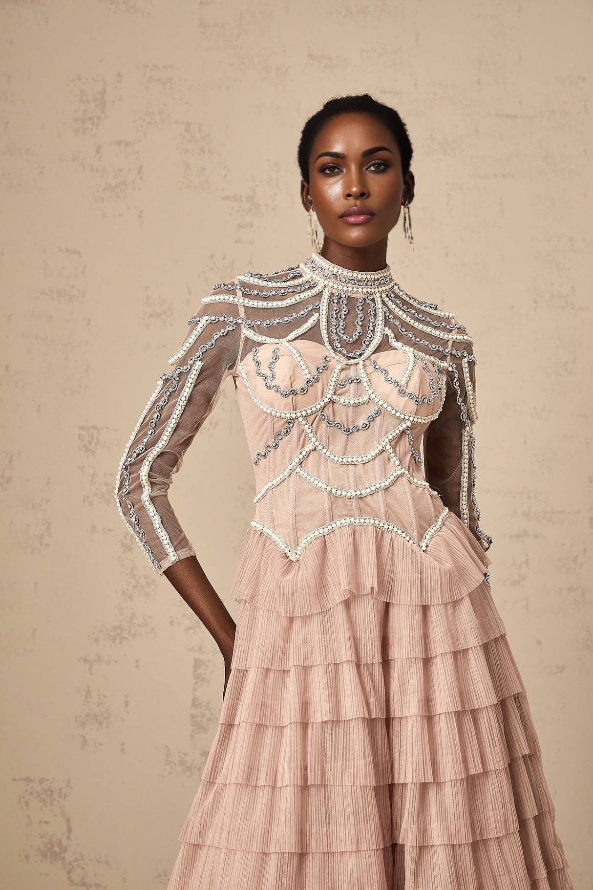 Woman wearing a long pink gown with tiered layers and beaded details flowing sheer fabric with a soft romantic look
