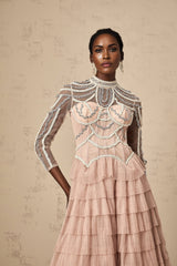 Woman wearing a long pink gown with tiered layers and beaded details flowing sheer fabric with a soft romantic look