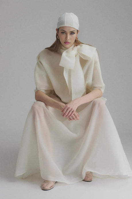 Woman wearing a long white maxi dress with ruffled details and a tie neck design