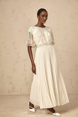 Woman wearing a long white pleated dress with crystal embellishments and flowing maxi skirt