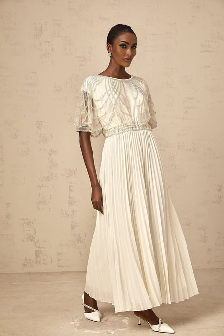 Woman wearing a long white pleated dress with crystal embellishments and flowing maxi skirt