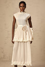 Woman wearing a long white sleeveless maxi dress with ruffles and pleats