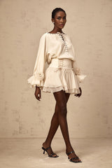Woman wearing a matching blouse and skirt set in light fabric with ruffles and self tie details