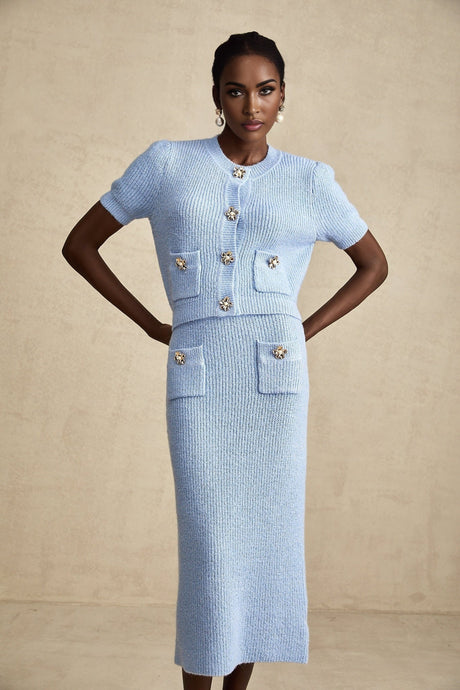 Woman wearing a matching blue knit blouse and skirt set standing against a plain background