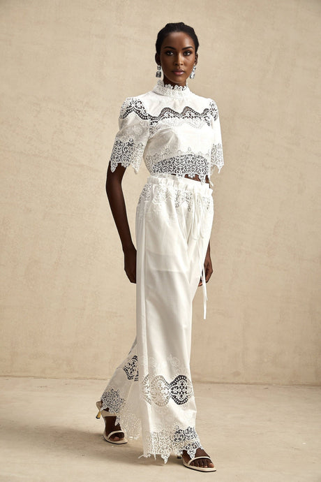 Woman wearing a matching set consisting of a cropped lace trim top with cutout details and coordinating trousers