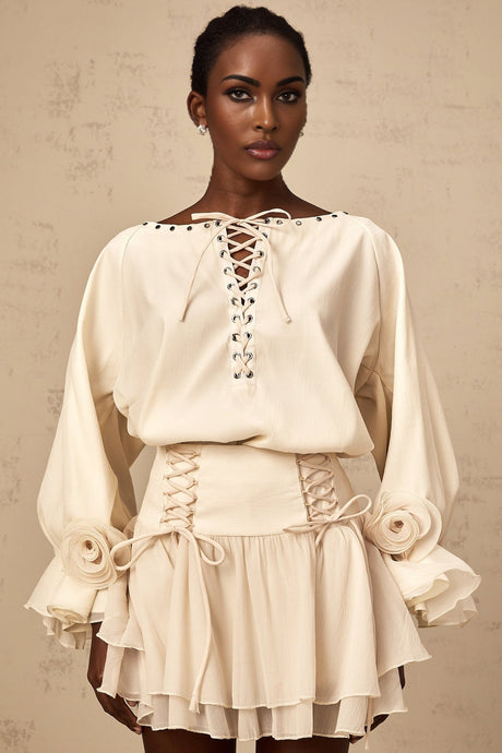 Woman wearing a matching set consisting of a light colored ruffled blouse with self tie details and a coordinating skirt standing against a plain background