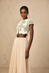 Woman wearing a matching set consisting of a light colored top and skirt with floral applique details in neutral tones