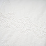 Woman wearing a matching set of white lace trim cropped top and trousers with cutout details