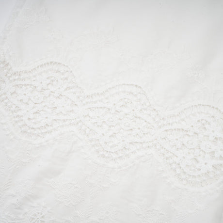 Woman wearing a matching set of white lace trim cropped top and trousers with cutout details