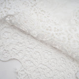 Woman wearing a matching set of white lace trimmed cropped top and trousers with cutout details
