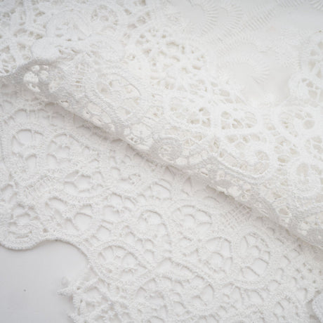 Woman wearing a matching set of white lace trimmed cropped top and trousers with cutout details