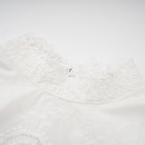 Woman wearing a matching set of white lace trimmed cropped top and trousers with cutout details