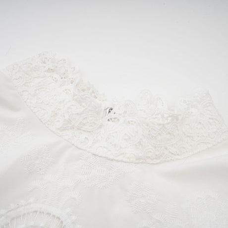 Woman wearing a matching set of white lace trimmed cropped top and trousers with cutout details