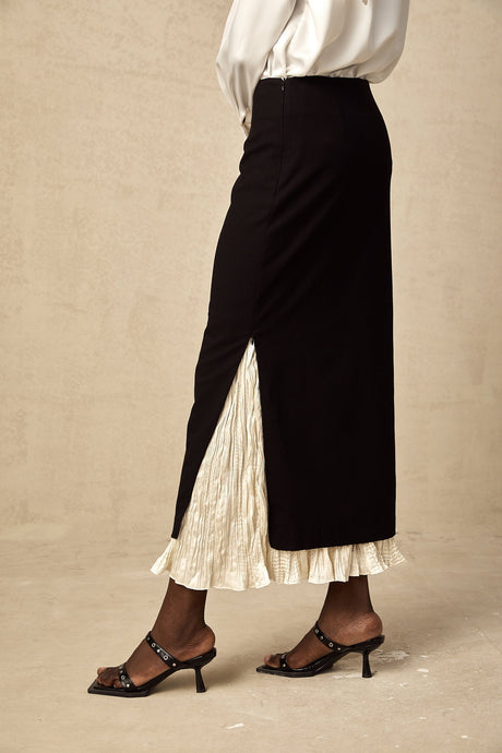 Woman wearing a midi length skirt with color blocked panels in contrasting shades standing against a plain background