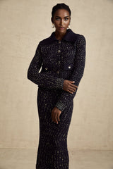 Woman wearing a navy blue crochet knit jacket and matching skirt set standing against a plain background