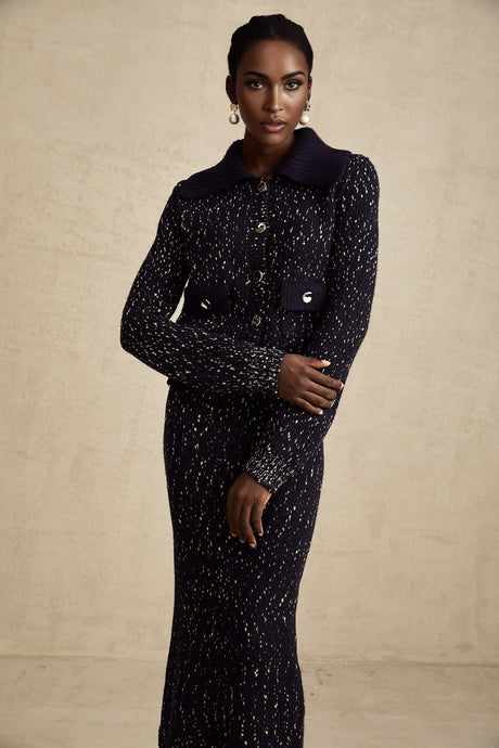 Woman wearing a navy blue crochet knit jacket and matching skirt set standing against a plain background