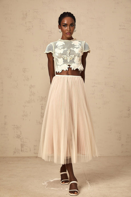 Woman wearing a neutral colored floral applique matching set with a top and skirt featuring delicate floral details