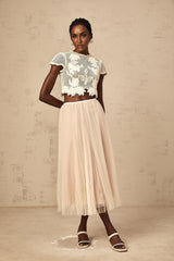 Woman wearing a neutral colored matching top and skirt set with floral applique details