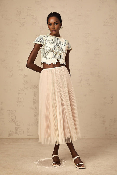 Woman wearing a neutral colored matching top and skirt set with floral applique details