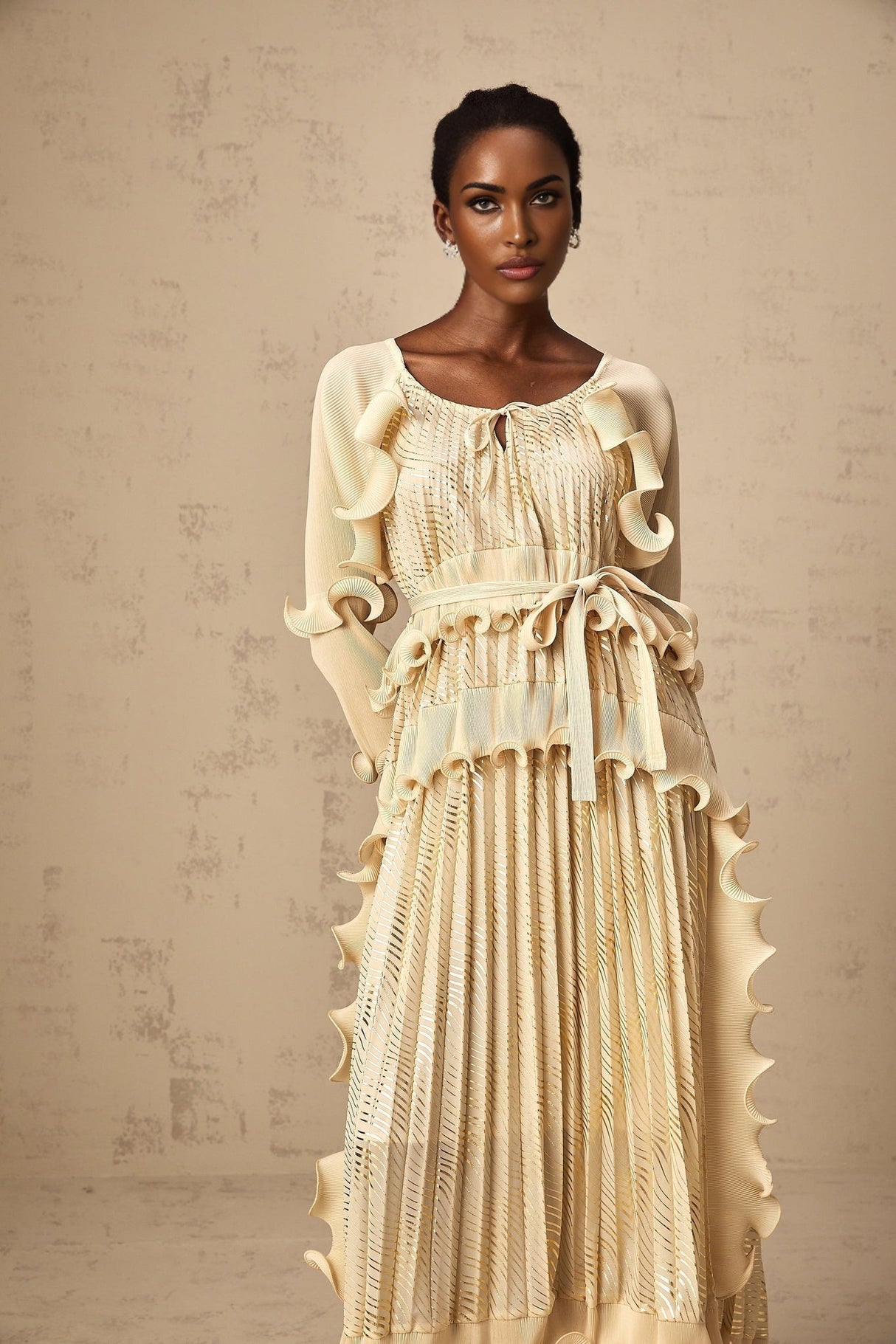 Woman wearing a neutral colored midi dress with gilded ruffles and a ruched bodice