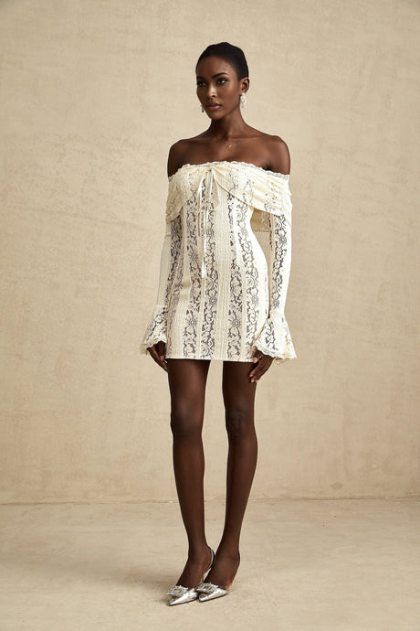 Woman wearing a neutral colored mini dress with floral lace pattern and flared cuffs
