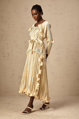 Woman wearing a neutral colored ruffled midi dress with gilded accents standing in a relaxed pose